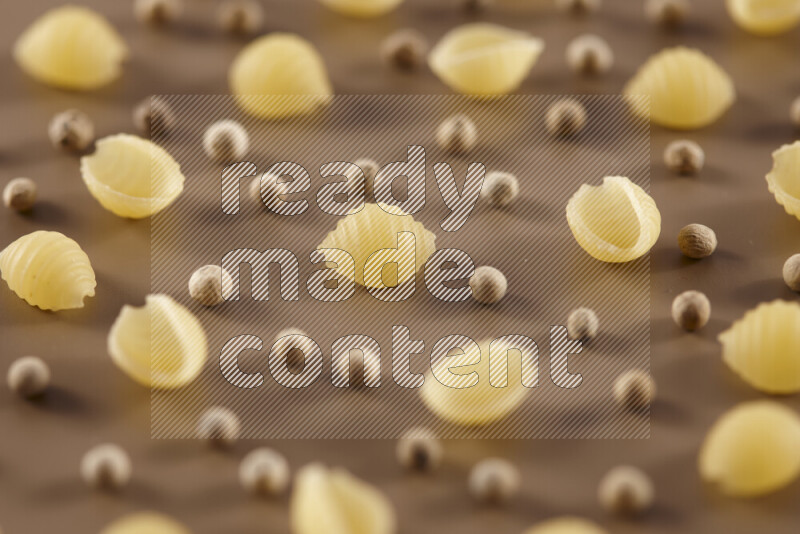 Raw pasta with different ingredients such as cherry tomatoes, garlic, onions, red chilis, black pepper, white pepper, bay laurel leaves, rosemary and cardamom on beige background