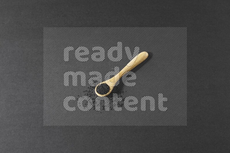 A wooden spoon full of black seeds and seeds spread beside it on a black flooring
