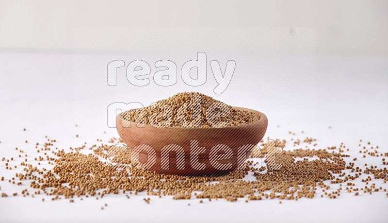 A wooden bowl full of mustard seeds and more seeds spread on a white flooring in different angles
