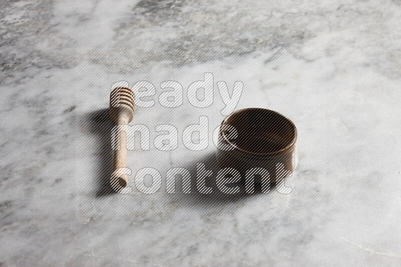 Brown pottery bowl with wooden honey dipper on the side on grey marble background