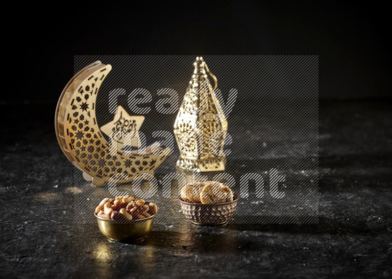Nuts in a metal bowl with dried figs beside golden lanterns in a dark setup