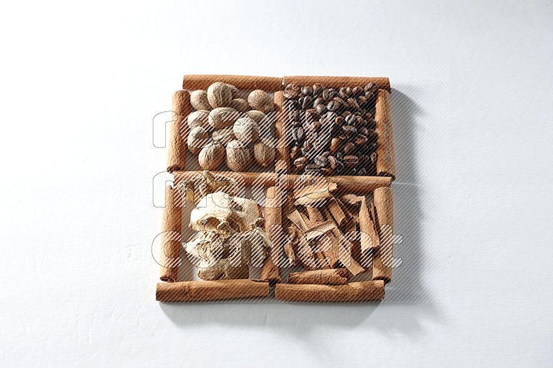 4 مربعات من أعواد القرفة ممتلئة بحبوب القهوة وجوزة الطيب والقرفة والزنجبيل المجفف على أرضية بيضاء
