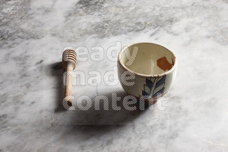 Decorative Pottery bowl with wooden honey handle on the side with grey marble flooring, 45 degree angle