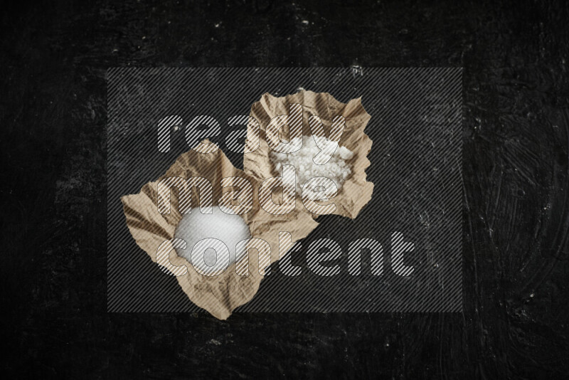 A crumpled piece of paper full of white salt on black background