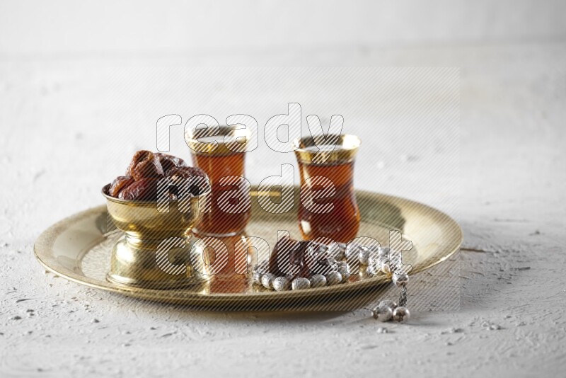 Dates in a metal bowl with tea and prayer beads on a tray in a light setup