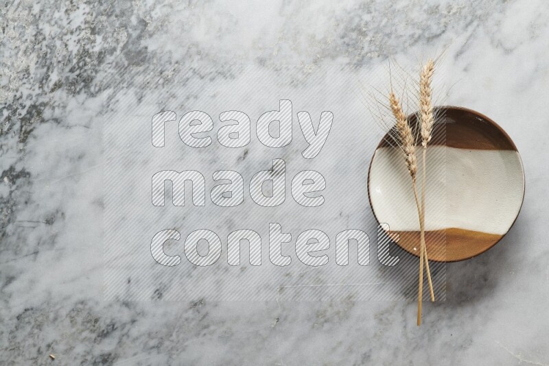 Wheat stalks on multicolored pottery plate on grey marble background