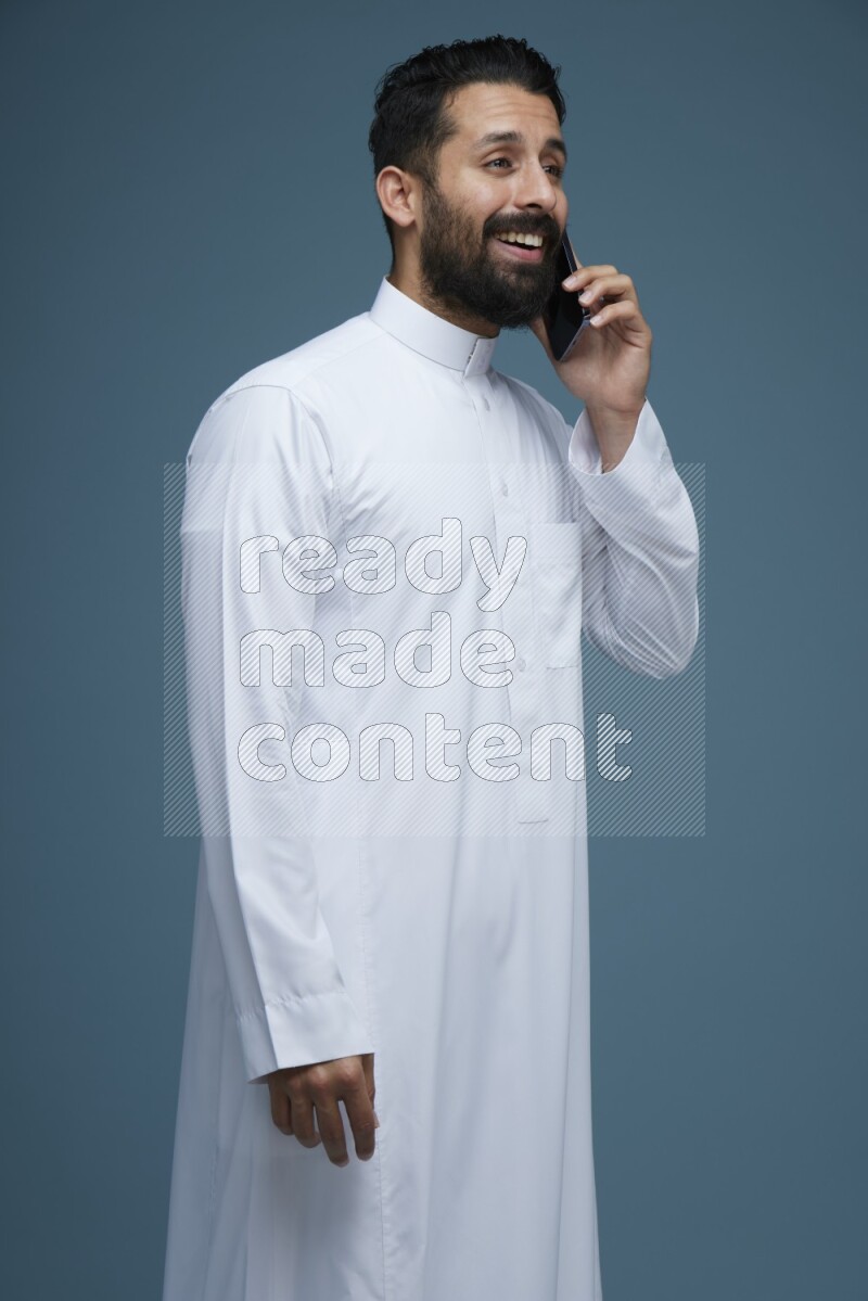 A man having a call on a blue background wearing Saudi Thob