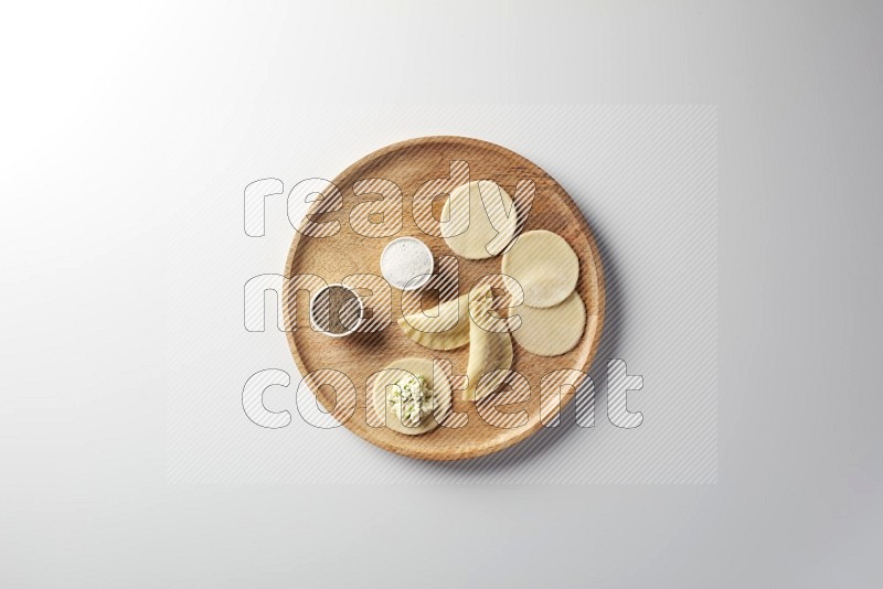 two closed sambosas and one open sambosa filled with cheese while salt, and black pepper aside in a wooden dish on a white background