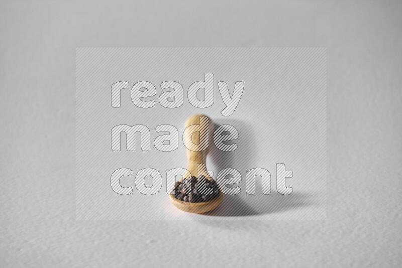 حبوب الفلفل الأسود في ملعقة خشبية علي خلفية بيضاء