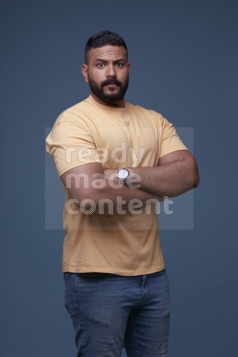 A man posing in a blue background wearing a yellow shirt