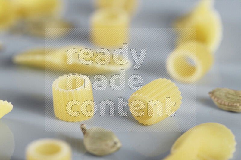 Raw pasta with different ingredients such as cherry tomatoes, garlic, onions, red chilis, black pepper, white pepper, bay laurel leaves, rosemary, cardamom and mushrooms on light blue background