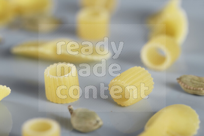 Raw pasta with different ingredients such as cherry tomatoes, garlic, onions, red chilis, black pepper, white pepper, bay laurel leaves, rosemary, cardamom and mushrooms on light blue background