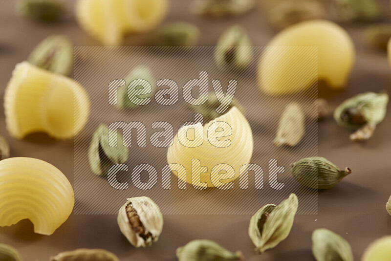 Raw pasta with different ingredients such as cherry tomatoes, garlic, onions, red chilis, black pepper, white pepper, bay laurel leaves, rosemary and cardamom on beige background