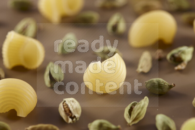 Raw pasta with different ingredients such as cherry tomatoes, garlic, onions, red chilis, black pepper, white pepper, bay laurel leaves, rosemary and cardamom on beige background