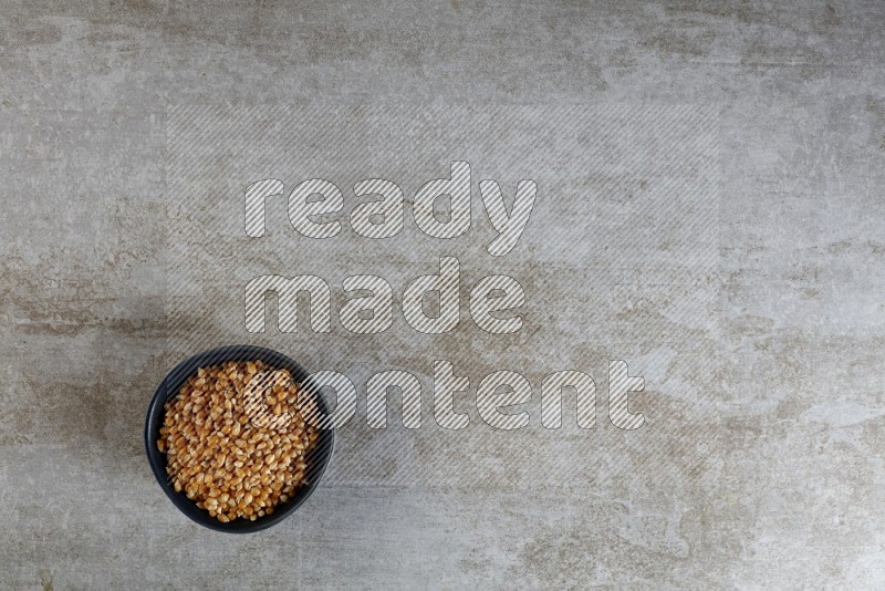 corn kernel in a black ceramic bowl on a grey textured countertop