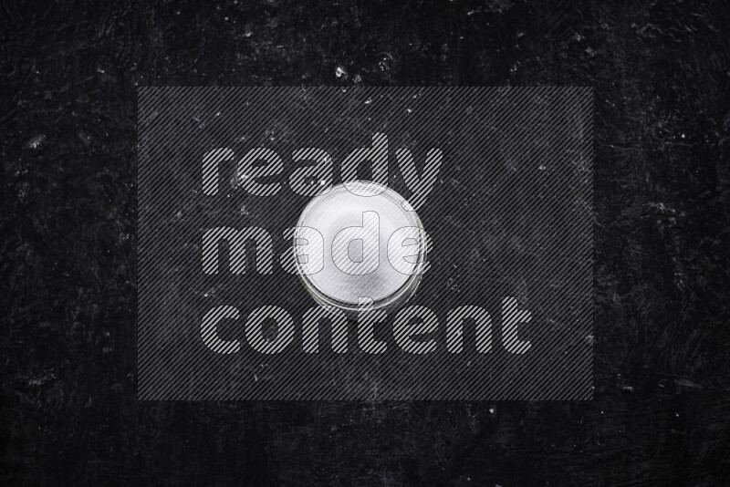 A glass jar full of fine table salt on black background