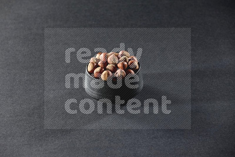 A black pottery bowl full of hazelnuts on a black background in different angles