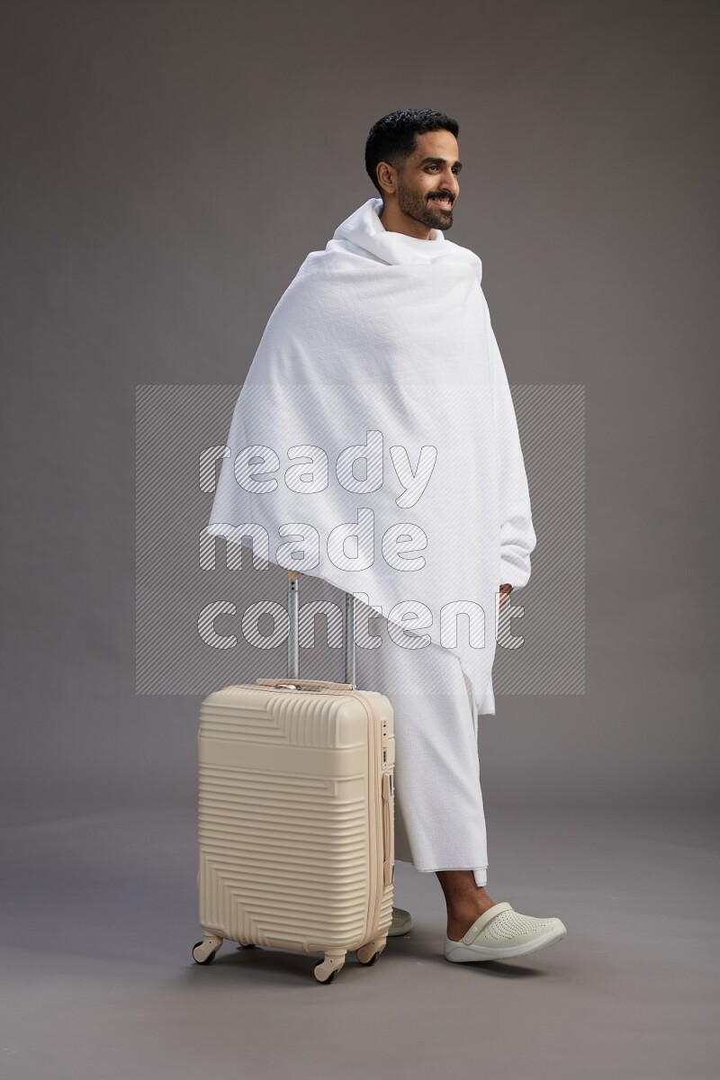 A man wearing Ehram Standing holding traveling bag on gray background