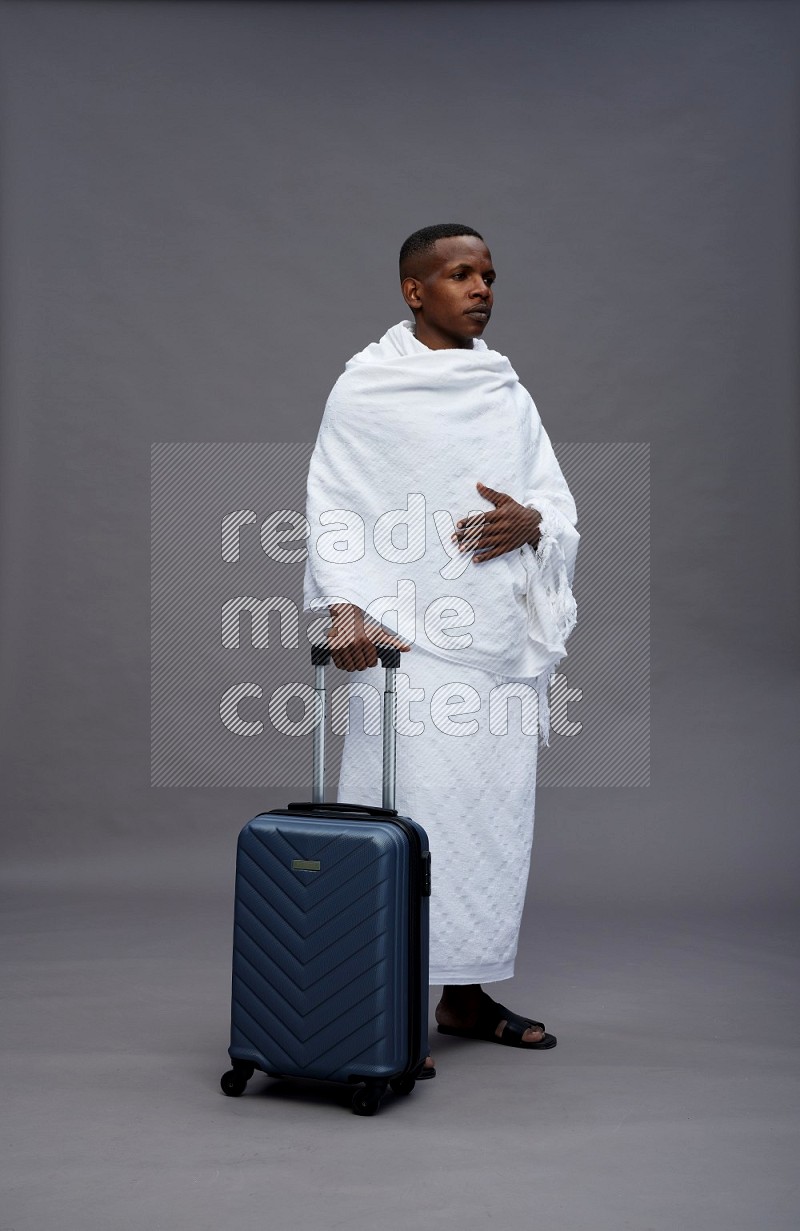 A man wearing Ehram Standing holding traveling bag on gray background