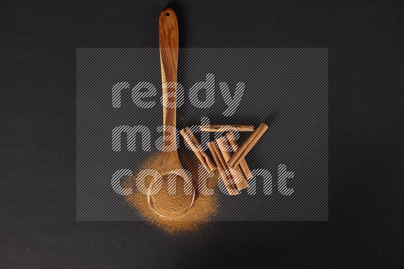 Cinnamon powder in a spoon ladle and spreaded on the floor beside it cinnamon sticks on the floor on black background in different angles