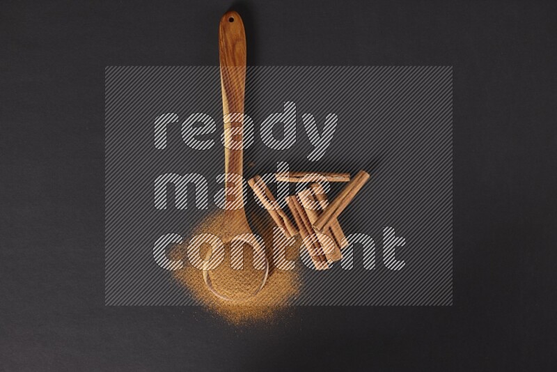 Cinnamon powder in a spoon ladle and spreaded on the floor beside it cinnamon sticks on the floor on black background in different angles