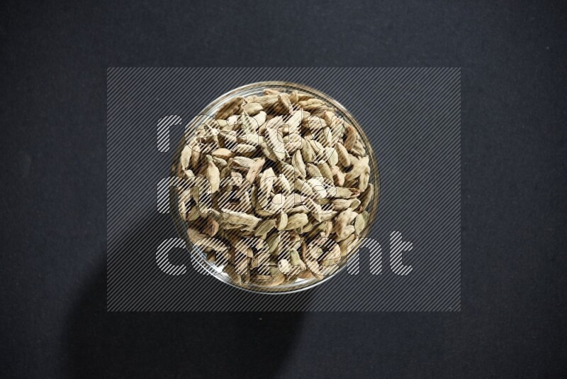 A glass bowl full of cardamom on black flooring