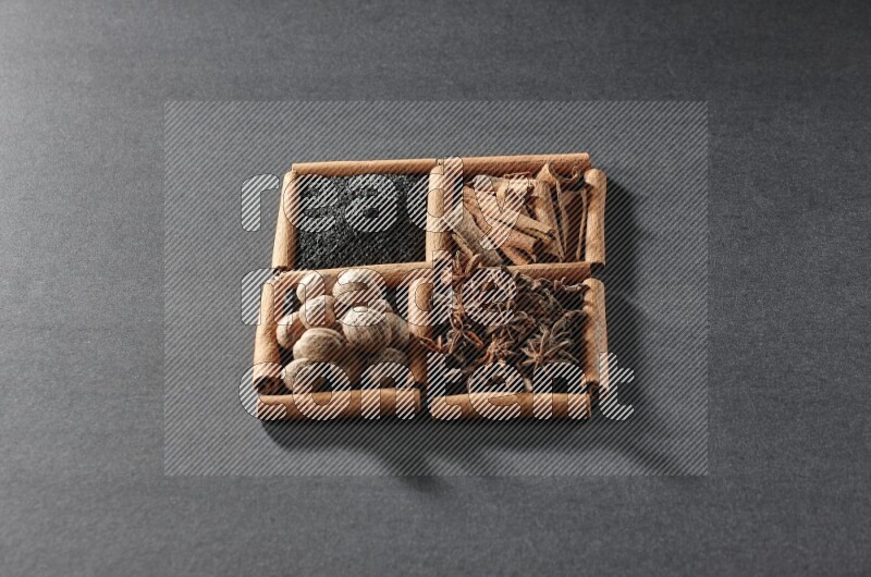 4 مربعات من عيدان القرفة ممتلئة بحبة البركة السوداء والقرفة واليانسون النجمي وجوزة الطيب على أرضية سوداء