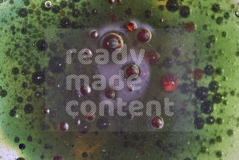 لقطات مقربة لقطرات ألوان مائية حمراء وخضراء وزرقاء على سطح الزيت على خلفية خضراء