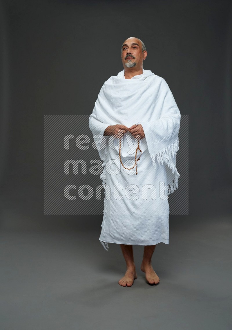 A man wearing Ehram Standing holding rosary on gray background