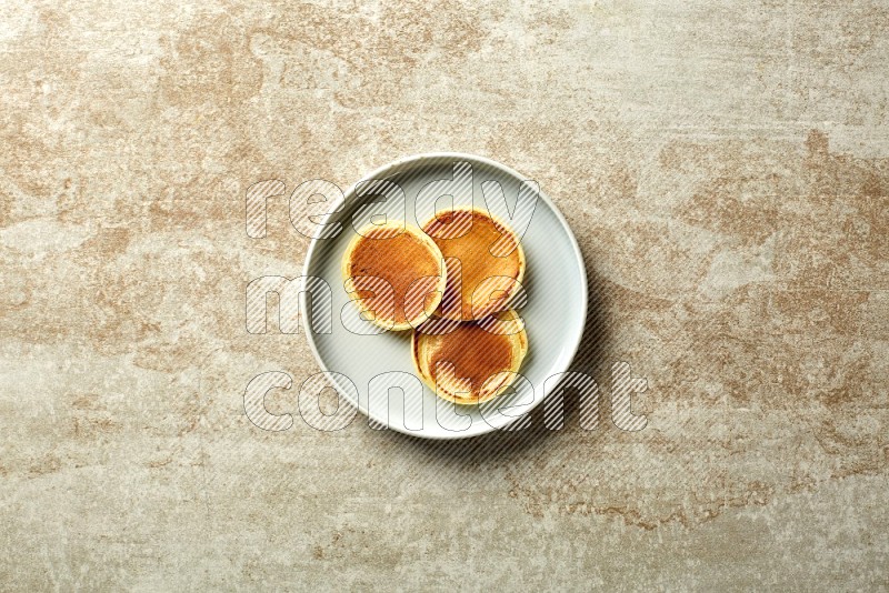 Three stacked plain mini pancakes in a blue plate on beige background