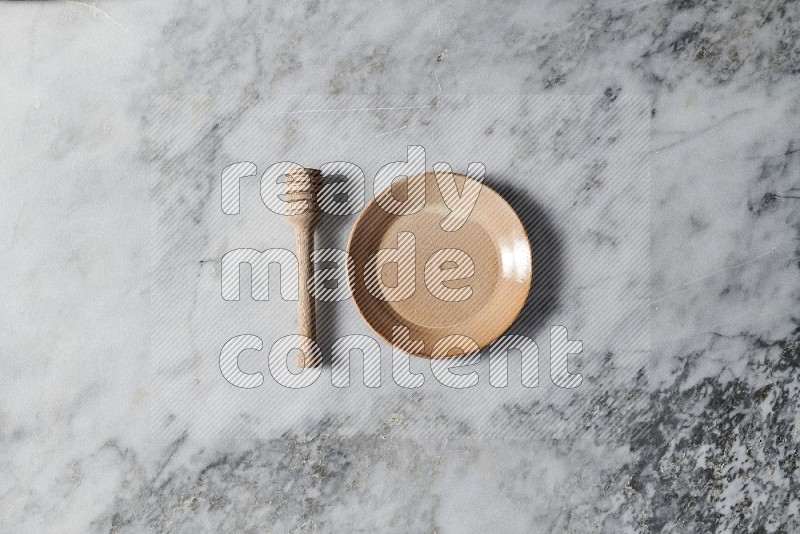 Beige Pottery Plate with wooden honey handle on the side on grey marble flooring, Top view