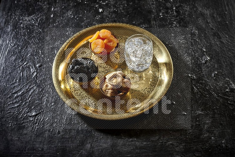 Dried fruits in metal bowls with water on a tray in dark setup