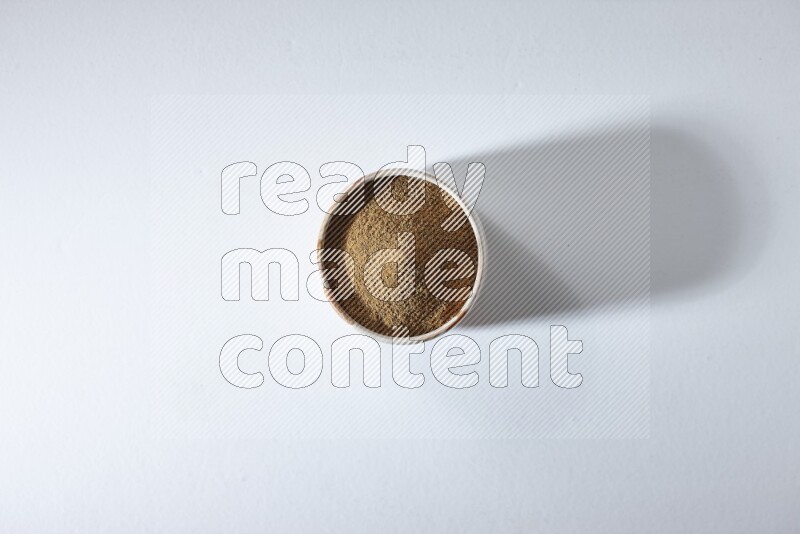 A beige bowl full of cumin powder on a white flooring