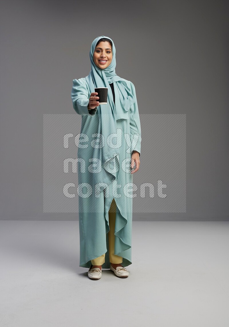 Saudi Woman wearing Abaya standing  holding paper cup on Gray background