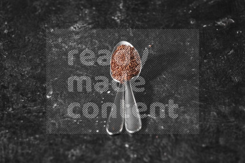 2 metal spoons full of garden cress seeds on a textured black flooring