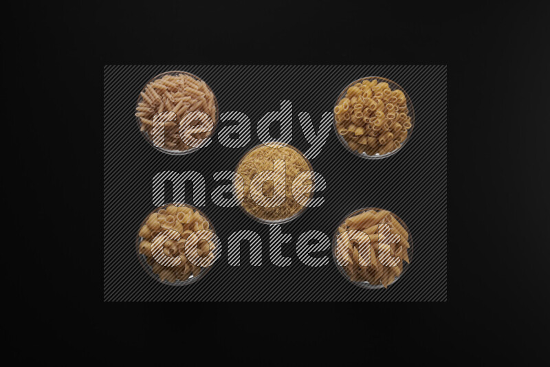 Different pasta types in 5 glass bowls on black background