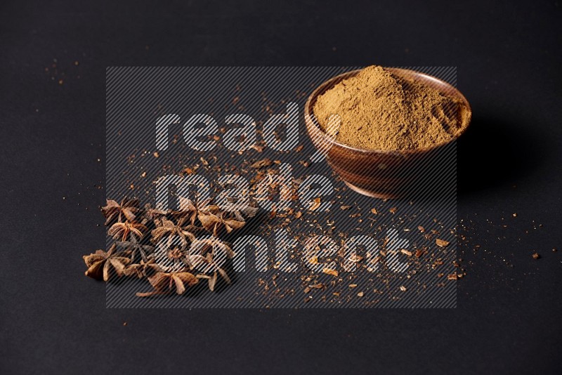Star Anise powder in a wooden bowl with star anise beside it on a black background