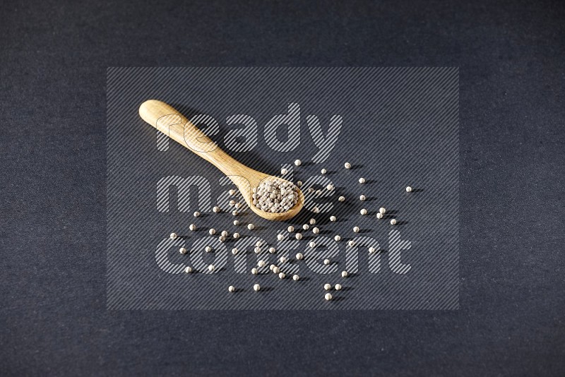 A wooden spoon full of white pepper beads on black flooring