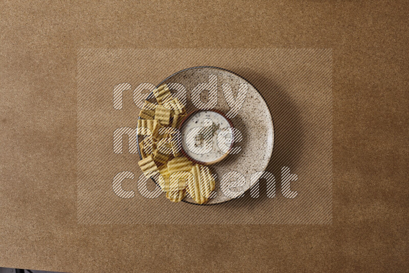 Assorted snacks on a pottery plate with a dipping on brown background