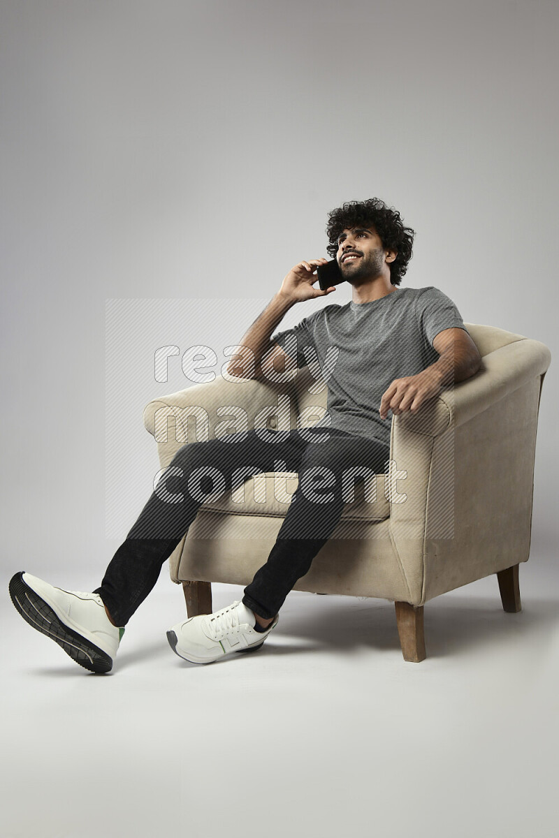 رجل يرتدي ملابس كاجوال يجلس علي كرسي و يتحدث في الهاتف علي خلفية بيضاء