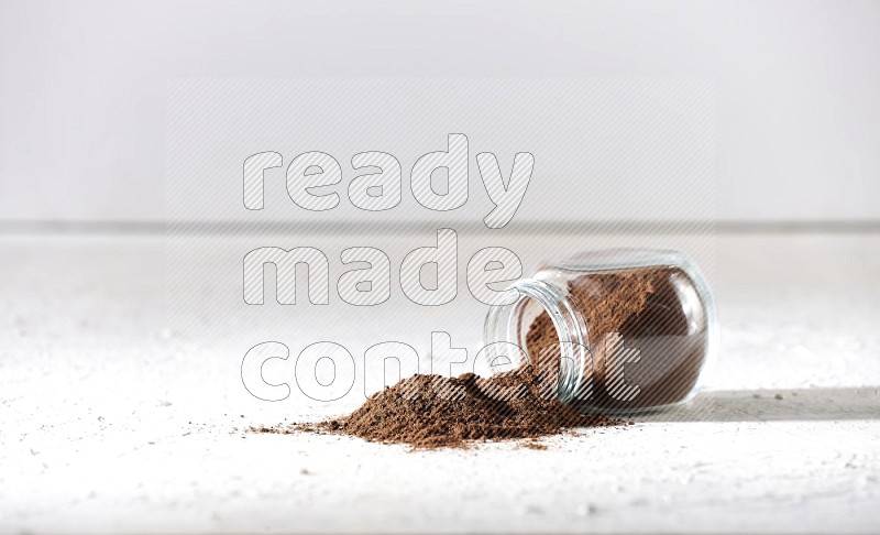 A flipped glass spice jar full of cloves powder and powder came out of it on textured white flooring