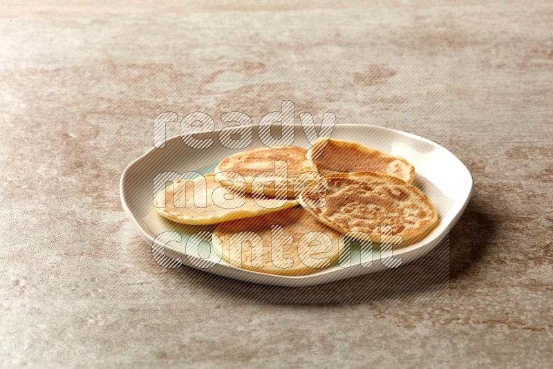 Five stacked plain mini pancakes in a bicolor plate on beige background