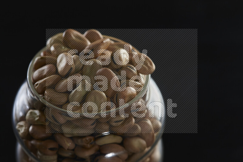 Fava beans in a glass jar on black background