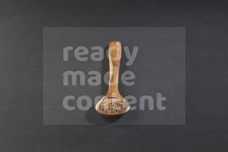 A wooden spoon full of mustard seeds on a black flooring