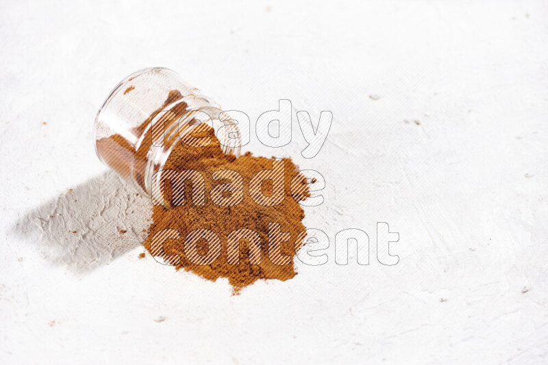 A glass jar full of ground paprika powder flipped with some spilling powder on white background