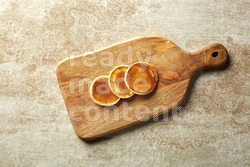 Three stacked plain mini pancakes on a wooden board on beige background