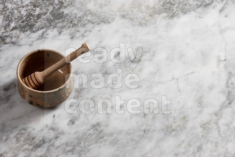 Multicolored Pottery bowl with wooden honey handle in it, on grey marble flooring, 65 degree angle