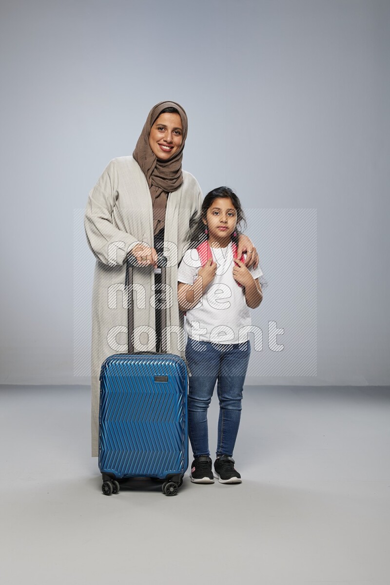 Mom and daughter standing pulling a carry-on bag on gray background