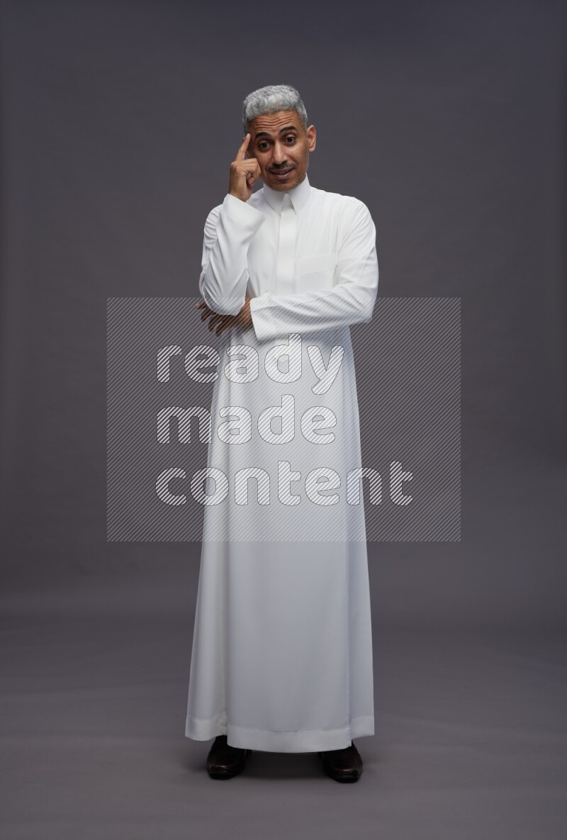 Saudi man wearing thob standing interacting with the camera on gray background