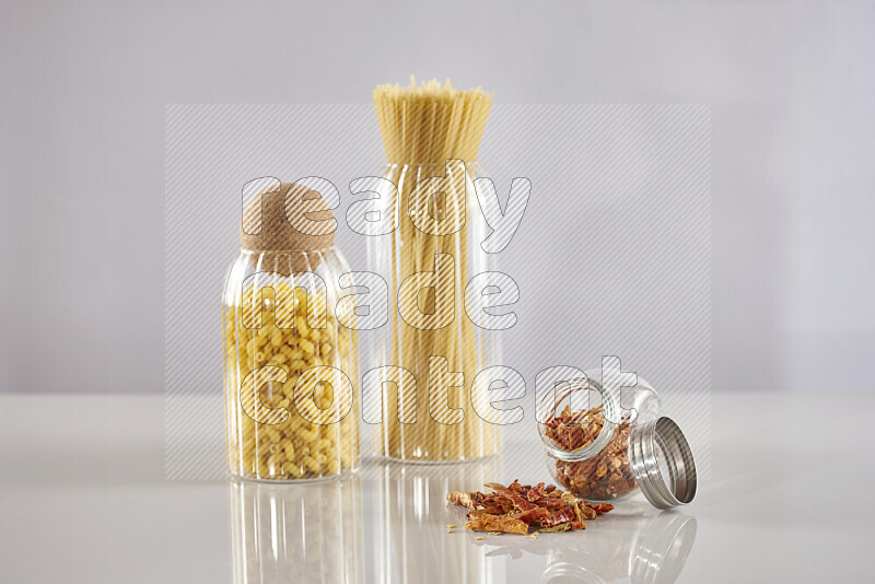 Raw pasta in glass jars with chilis on light grey background
